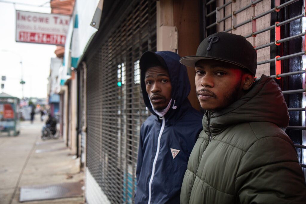 Image from iOS (1) Two young Black men standing in front of a storefront.