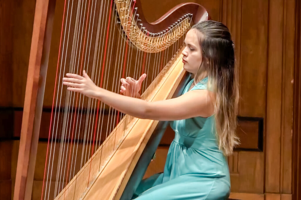 Claire Thai wearing a teal dress playing the harp on stage