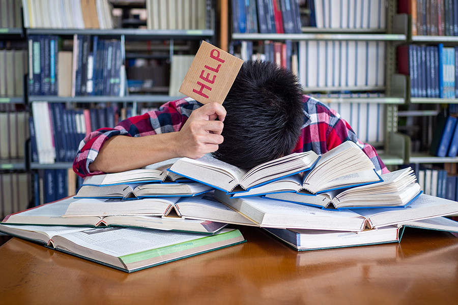 Asian Male Students Are Tired And Stressed With Reading A Lot To A tired and stressed student with his head down on a pile of books holding up a