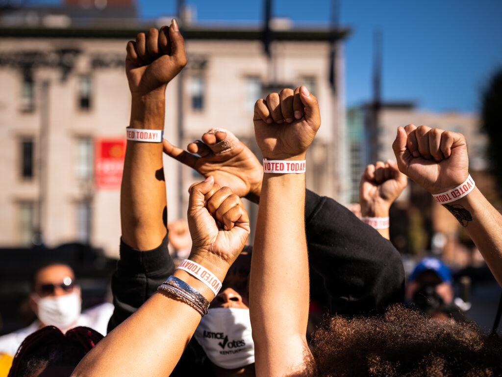 Black Lives Matter protesters display wristbands reading “I VOTED”. Activists warn Black and Latino voters are being flooded with disinformation intended to suppress turnout in the election’s final days. Black Lives Matter protests fists in the air