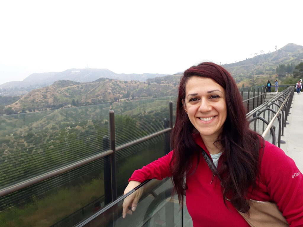 valentina-graci Woman with long reddish hair and a red shirt smiles by a scenic overlook