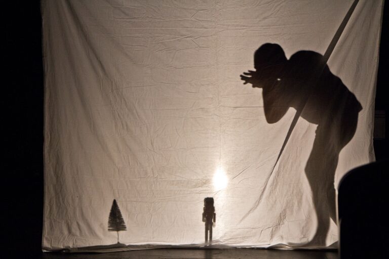 Shadows behind a sheet show a person creeping foward, a tiny figure of a person, and a tiny figure of a tree