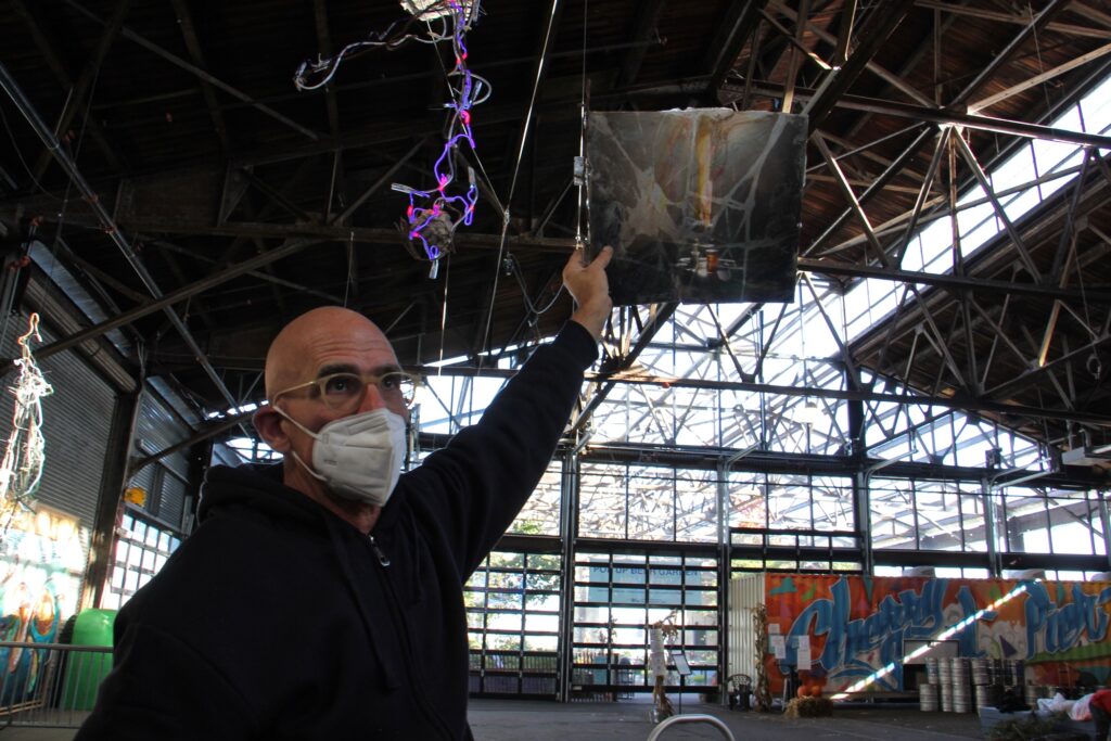 2020 11 05-e lee-John Schlesinger-philadelphia cherry street pier-sculptural exhibit broken painting John Schlesinger holds a still life painting, broken and repaired, up to the light at the Cherry Street Pier. The work produces the desired effect when lit from behind. (Emma Lee/WHYY)