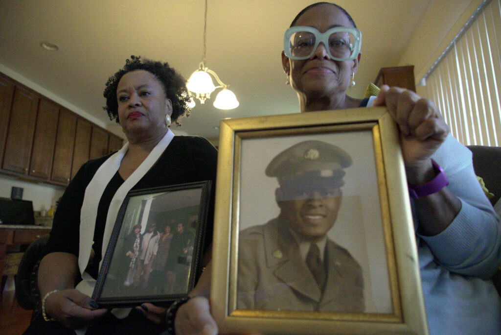 Virus Outbreak-Nursing Home Neglect Sisters Barbara Leak-Watkins, right, and Alberta Lynn Fantroy pose with photos of their late father, Alex Leak Jr., at Watkins’ home in Greensboro, N.C., on Wednesday, Nov. 4, 2020. The Army veteran died in July after collapsing from dehydration at his assisted living facility, and the family believe pandemic-related neglect is to blame. (AP Photo/Allen G. Breed)
