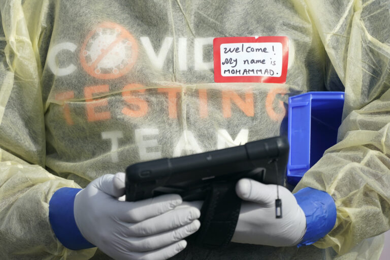 A worker wearing gloves, and other PPE holds a tablet computer as he waits to check people in, Wednesday, Oct. 28, 2020, at a King County coronavirus testing site in Auburn, Wash., south of Seattle. (AP Photo/Ted S. Warren)