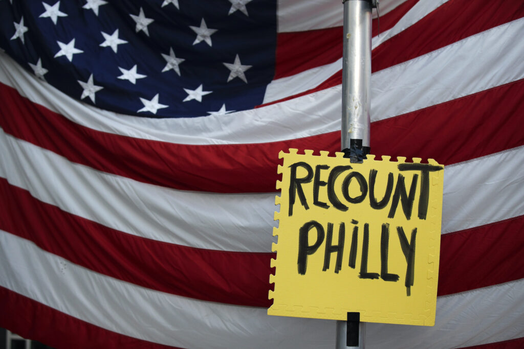 Election 2020 Protests Philadelphia A sign hangs in front of an American flag, as a handful of supporters of President Donald Trump continue to protest outside the Pennsylvania Convention Center, in Philadelphia, Tuesday, Nov. 10, 2020. (AP Photo/Rebecca Blackwell)