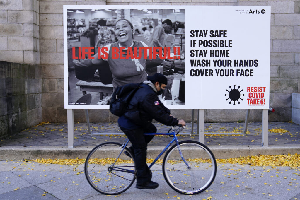 A man wearing a face mask bicycles along Broad Street, Wednesday, Nov. 18, 2020, in Philadelphia. (AP Photo/Matt Slocum)
