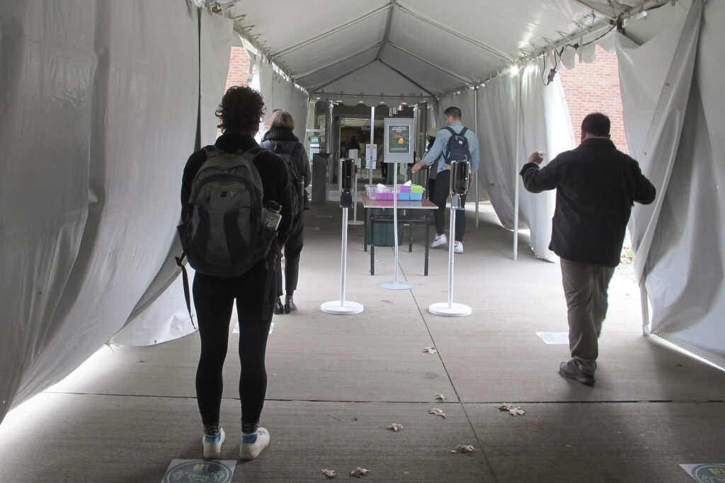Virus Outbreak Colleges In this Nov. 12, 2020, photo, University of Vermont students walk through a tent leading to a COVID-testing site on campus in Burlington, Vt. As coronavirus cases are surging around the U.S., some colleges and universities are rethinking some of their plans for next semester. (AP Photo/Lisa Rathke)