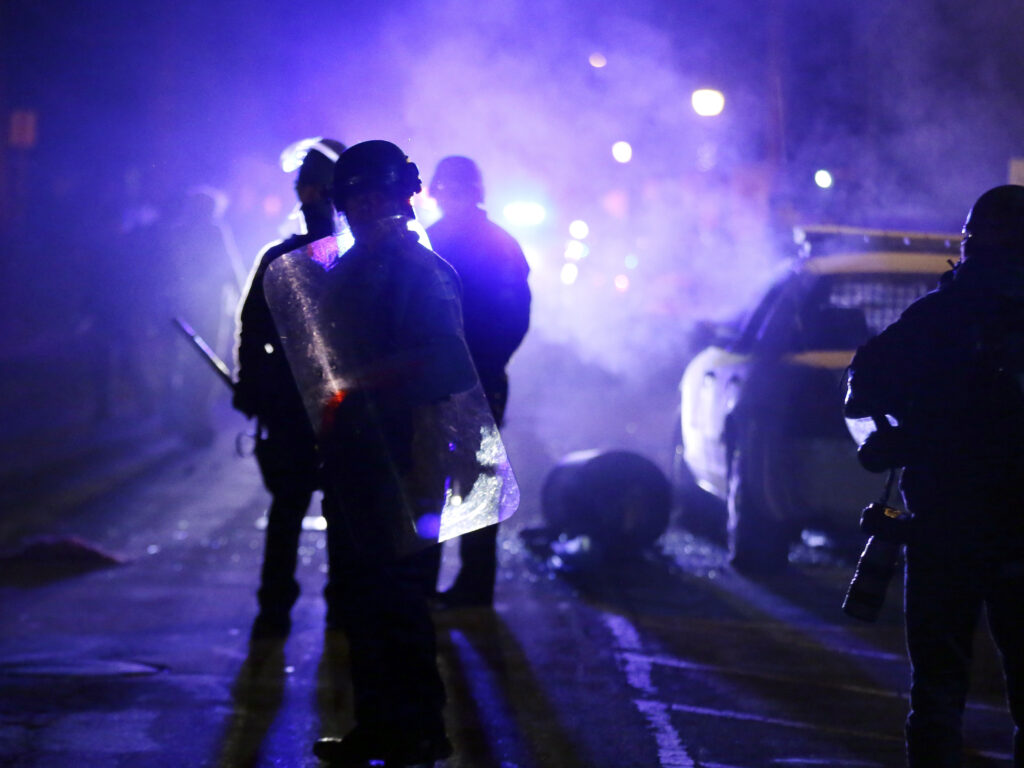 Police officers in Ferguson, Mo., during a protest in 2014. Advocates want the Justice Department to step up its oversight of law enforcement in the incoming administration. Police officers watch protesters as smoke fills the streets in Ferguson, Mo.