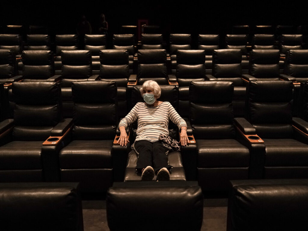 A woman sits in a theater in Irvine, Calif., waiting for a movie to start, on Sept. 8. A COVID-19 vaccine could unleash pent-up spending from households that have mostly avoided activities like going to the gym during the coronavirus pandemic. A woman sits in a theater in Irvine, Calif., waiting for a movie to start, on Sept. 8. A COVID-19 vaccine could unleash pent-up spending from households that have mostly avoided activities like going to the gym during the coronavirus pandemic. (Jae C. Hong/AP Photo)