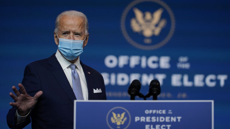 Joe Biden stands at a podium wearing a face mask