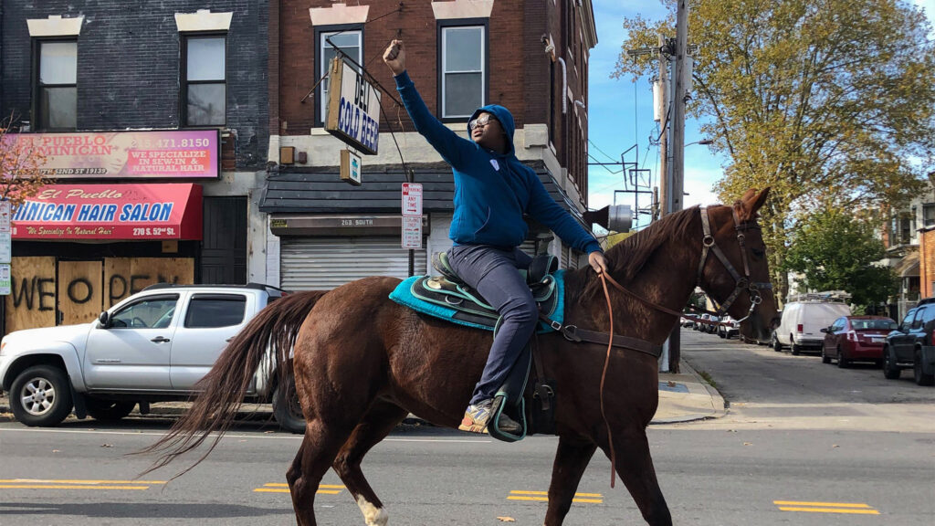 fletcherstreet-gotv-rumorsofwar-02crop 13-year-old Nahye Hyman raises a fist on his horse Sally during a GOTV ride down 52nd Street LAYLA A. JONES / BILLY PENN