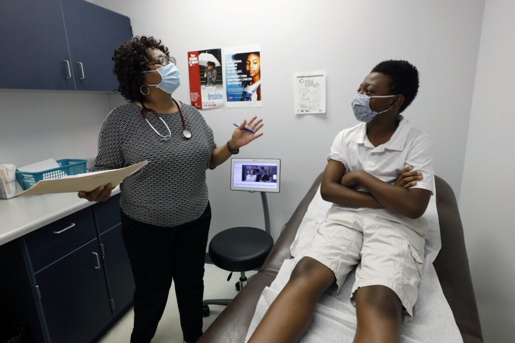 AP20237468054399-1920×1280 Jeremiah Young, 11, right, listens as Dr. Janice Bacon, a primary care physician, with Central Mississippi Health Services explains the necessity of receiving inoculations prior to attending school, Aug. 14, 2020, while at the Community Health Care Center on the Tougaloo College campus in Tougaloo, Miss. (Rogelio V. Solis/AP Photo)