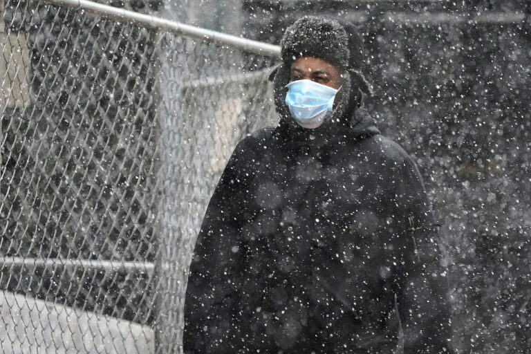 A man wearing a mask walks through a mid-afternoon snow squall in downtown Pittsburgh on Tuesday, Nov. 17, 2020. (AP Photo/Gene J. Puskar)
