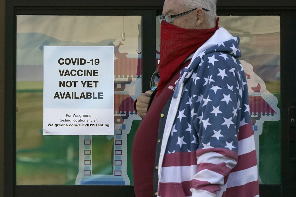 A pedestrian wearing a mask walks past a sign advising that COVID-19 vaccines are not available yet at a Walgreen’s pharmacy store during the coronavirus outbreak in San Francisco, Wednesday, Dec. 2, 2020. (AP Photo/Jeff Chiu)