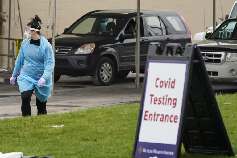 A health care worker walks past some of the vehicles lined up for COVID-19 testing at a drive-thru site, Friday, Dec. 4, 2020, in Butler, Pa. (AP Photo/Keith Srakocic)