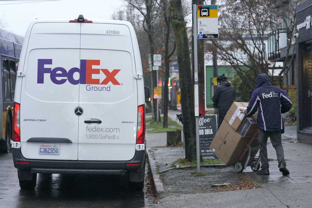 Virus Outbreak Holiday Shipping A driver with FedEx carries a package away from a van, Tuesday, Dec. 8, 2020, in Seattle. Store are warning online shoppers that if holiday purchases aren't made soon, they may not be delivered in time for Christmas. (AP Photo/Ted S. Warren)