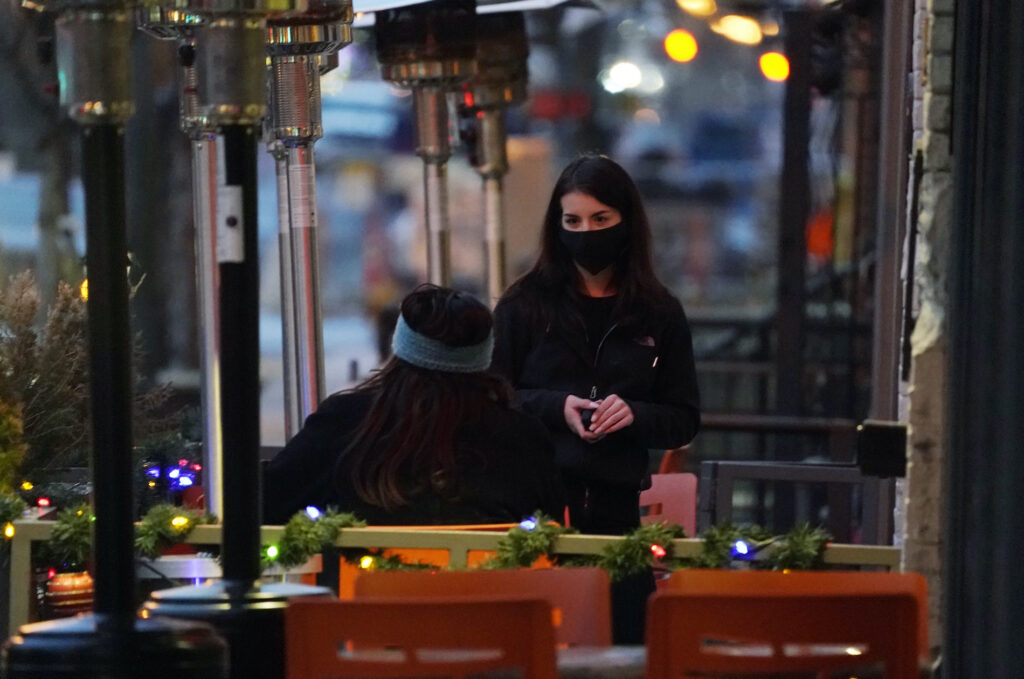 Virus Outbreak Colorado A waitperson wears a face mask while tending to a patron sitting in the outdoor patio of a sushi restaurant late Monday, Dec. 28, 2020, in downtown Denver. (AP Photo/David Zalubowski)