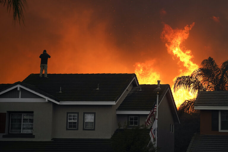Herman Termeer, 54, stands on the roof of his home as the Blue Ridge Fire burns along the hillside in Chino Hills
