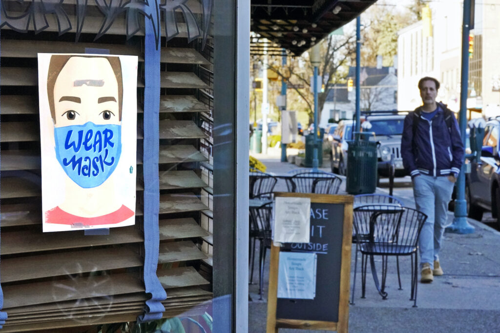 Virus Outbreak Pennsylvania A man walks past a restaurant in Mount Lebanon, Pa., with a sign in the window that reminds people to wear a mask