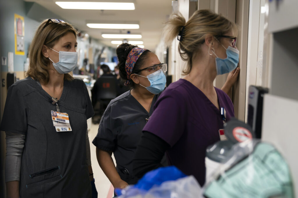 AP_coronavirus_hospital_workers_122120 Registered nurse Kristina Shannon, from left, chaplain Andrea Cammarota, and ER charge nurse Cathy Carter watch as medical workers try to resuscitate a patient who tested positive for coronavirus in the emergency room