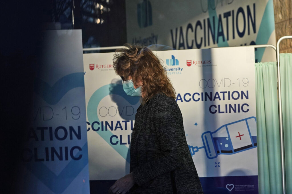 Virus Outbreak New Jersey A woman stands near signs at University Hospital's COVID-19 vaccine clinic at Rutgers New Jersey Medical School in Newark