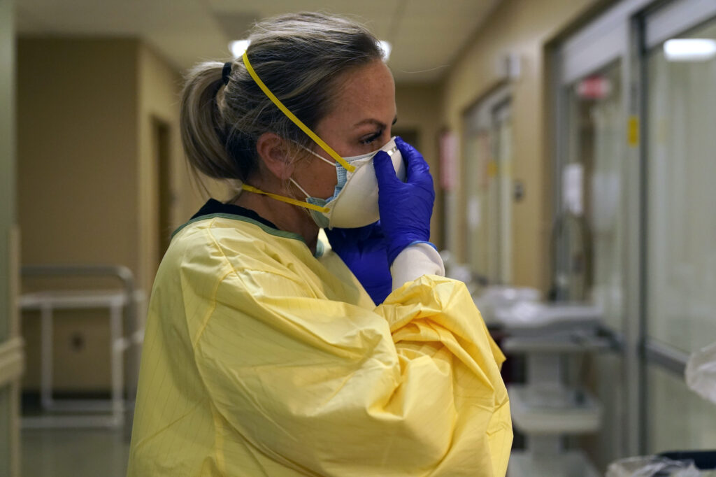 Virus Outbreak US Surge Registered nurse Chrissie Burkhiser puts on personal protective equipment as she prepares to treat a COVID-19 patient in the in the emergency room