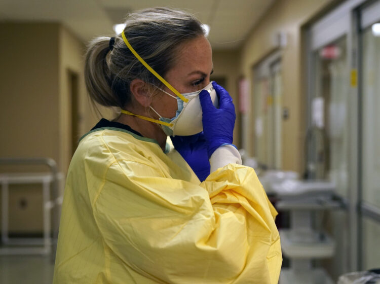 Registered nurse Chrissie Burkhiser puts on personal protective equipment as she prepares to treat a COVID-19 patient in the in the emergency room