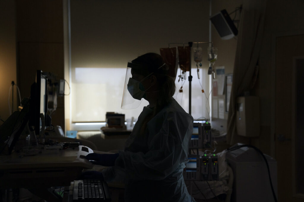 Virus Outbreak US Surge A a registered nurse works on a computer while assisting a COVID-19 patient