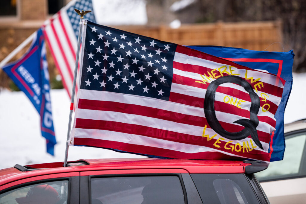 gettyimages-1229621342_slide-7b4e0a19a4f42c09a601a1b122cf76afee36a6ad-s1600-c85 A car with a flag endorsing the QAnon conspiracy theory drives by as supporters of President Donald Trump gather for a rally outside the Governor's Residence on Nov. 14 in St. Paul, Minn