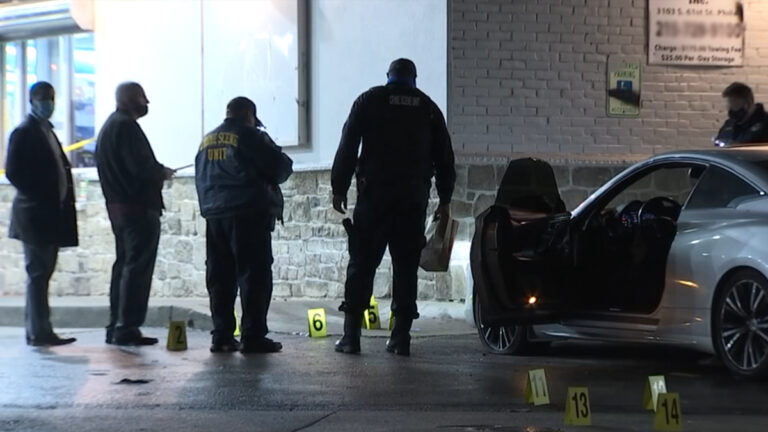 Detectives look at the ground as evidence markers lay on the ground surrounding a vehicle following a fatal carjacking in North Philadelphia.