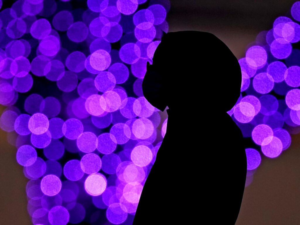 Political divisions over the pandemic are creating a wedge and splitting off health care workers from small communities that desperately need them. A woman wears masks to prevent the spread of the coronavirus as she looks at a holiday display