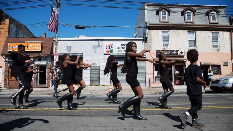 The Mass Konfusion drill team makes their way down Woodland Avenue as a Liberian flag hangs above the street at Southwest Pride Day in 2017. (Annie Risemberg for WHYY)