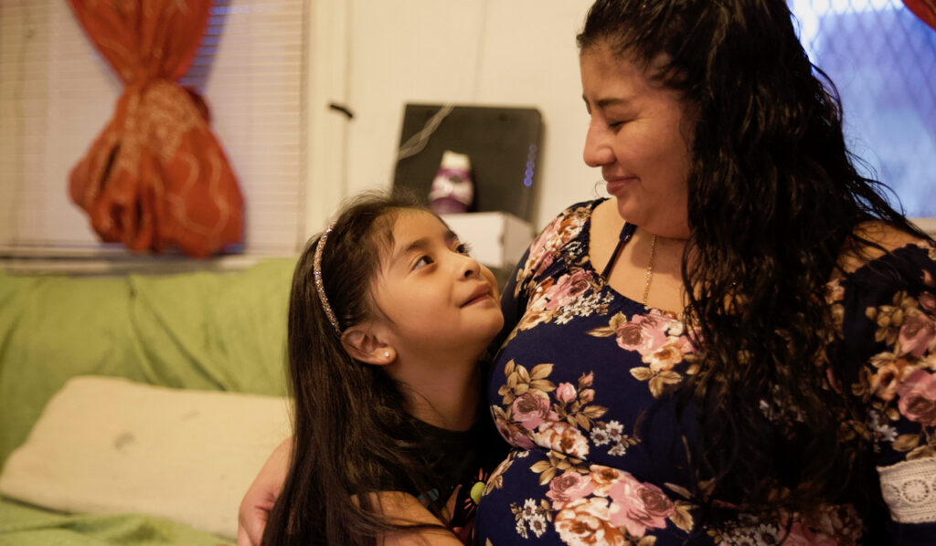 4I2C3309-2 Marta and her daughter, Krishna, hug one another lovingly in their living room. Marta was only able to bring Krishna to the United States, leaving her two sons behind in Guatemala. | Marta y su hija, Krishna, se abrazan en su sala de estar. Marta solo pudo traer a Krishna a los Estados Unidos, dejando a sus dos hijos en Guatemala. (Tony Rocco/WHYY)