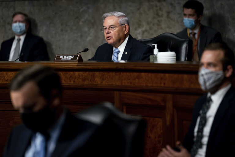 Sen. Menendez sits at a mahogany bench, speaking into a microphone.