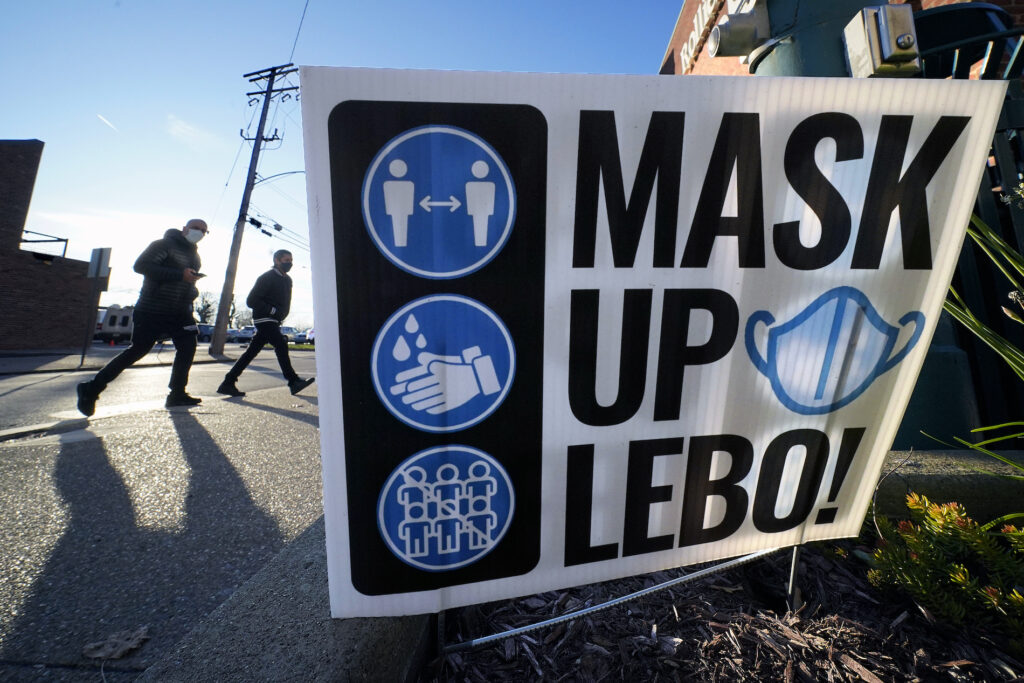 Virus Outbreak Pennsylvania Pedestrians walk past a sign on in Mount Lebanon, Pa.,reminding people to wear a mask, wash their hands and practice social distancing, Wednesday, Nov. 18, 2020. (AP Photo/Gene J. Puskar)