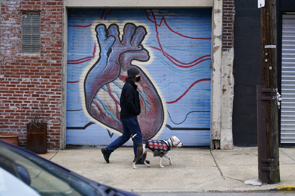Virus Outbreak Pennsylvania A man wearing a face mask to protect against the spread of the coronavirus walks with a dog, Wednesday, Dec. 9, 2020, in Northeast Philadelphia. (AP Photo/Matt Slocum)
