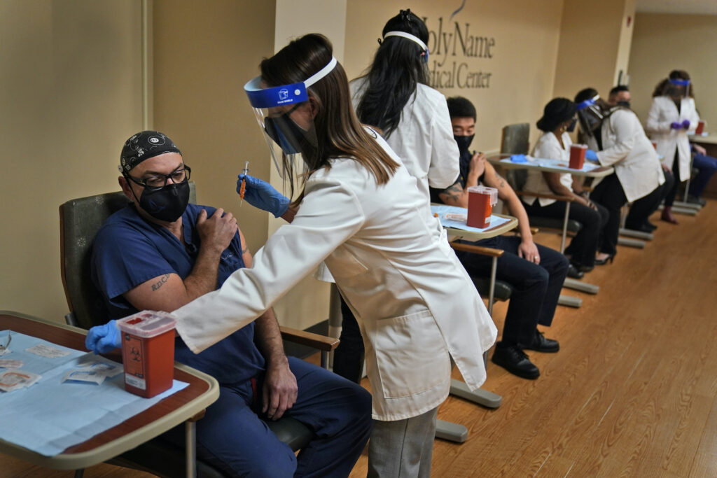 Virus Outbreak New Jersey Nurse Reynaldo Pella, left, was one of five staff members to simultaneously receive the first doses of the COVID-19 vaccine at Holy Name Medical Center in Teaneck, N.J., Thursday, Dec. 17, 2020. The hospital received almost 1000 doses of the vaccine in the middle of a snowstorm which blanketed much of the Northeast in snow. (AP Photo/Seth Wenig)