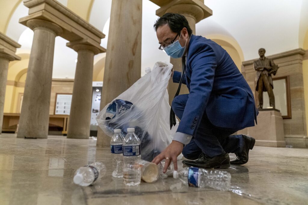 Rep. Andy Kim, D-N.J., cleans up debris and trash strewn across the floor in the early morning hours after protesters stormed the Capitol in Washington, Thursday, Jan. 7, 2021. (AP Photo/Andrew Harnik)