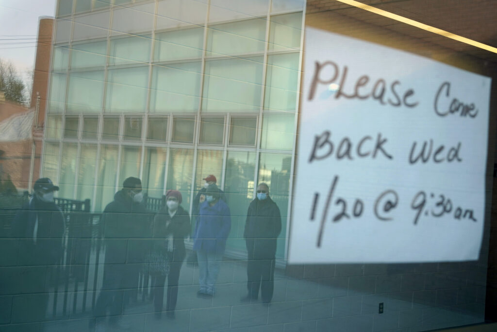 Virus Outbreak New Jersey People waiting in line are reflected in the glass windows of a vaccination site in Paterson, N.J., Tuesday, Jan. 19, 2021. A sign on the door of the vaccination site, which takes walk-ins rather than appointments, said it would be open tomorrow. (AP Photo/Seth Wenig)
