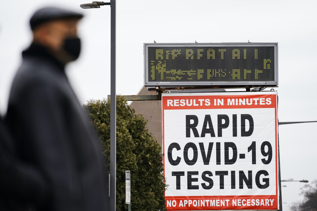 Virus Outbreak Pennsylvania A person wearing a face mask as a precaution against the coronavirus stands near a sign advertising a rapid COVID-19 testing site in Philadelphia, Monday, Jan. 25, 2021. (AP Photo/Matt Rourke)