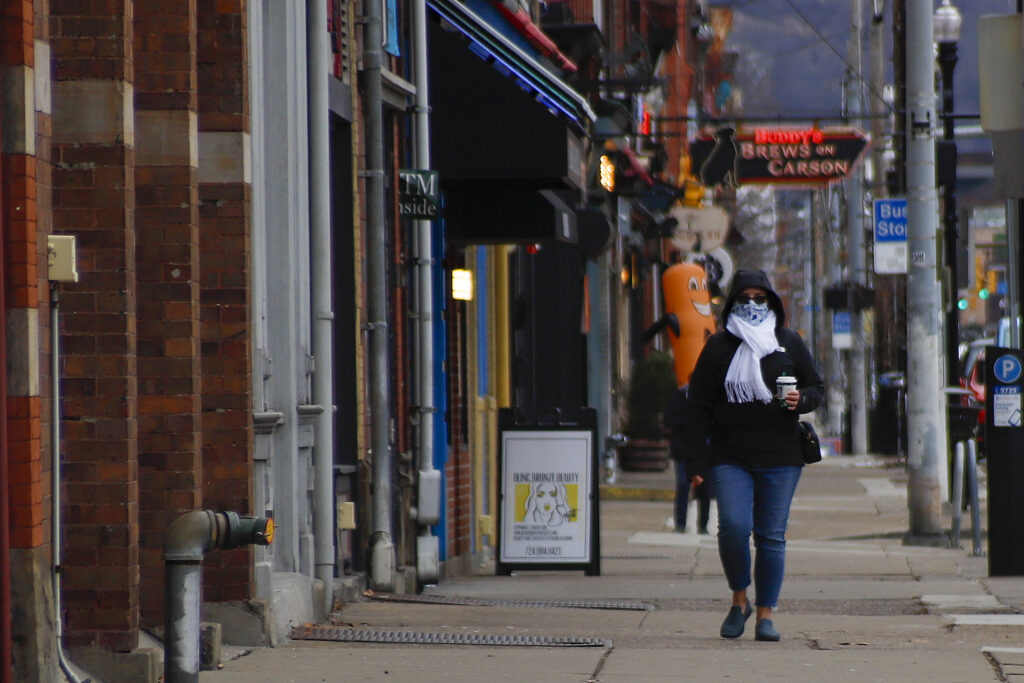 Virus Outbreak Pennsylvania People wearing protective masks walk past businesses and apartments along East Carson Street