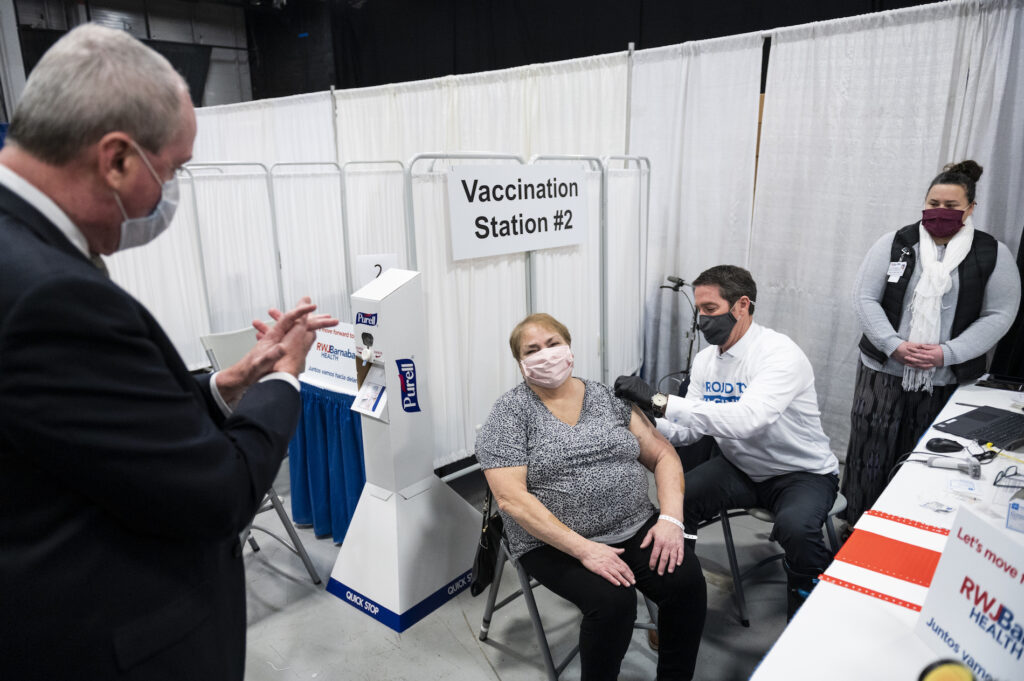 Governor Murphy Visits Middlesex Countyís Covid-19 Vaccination ‘Megasite’ Phil Murphy, New Jersey's governor, left, applauds after a person receives a dose of a Covid-19 vaccination at the New Jersey Convention and Exposition Center in Edison, New Jersey, U.S., on Friday, Jan. 15, 2021. New Jersey will expand Covid-19 vaccinations to people 65 years old and over and those ages 16 to 64 who have