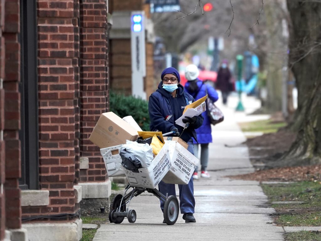 A U.S. postal worker delivers packages, boxes and letters in Chicago’s Hyde Park neighborhood shortly before Christmas. The U.S. Postal Service said it faces “unprecedented volume increases and limited employee availability due to the impacts of COVID-19.” A U.S. postal worker delivers packages, boxes and letters on the sidewalk