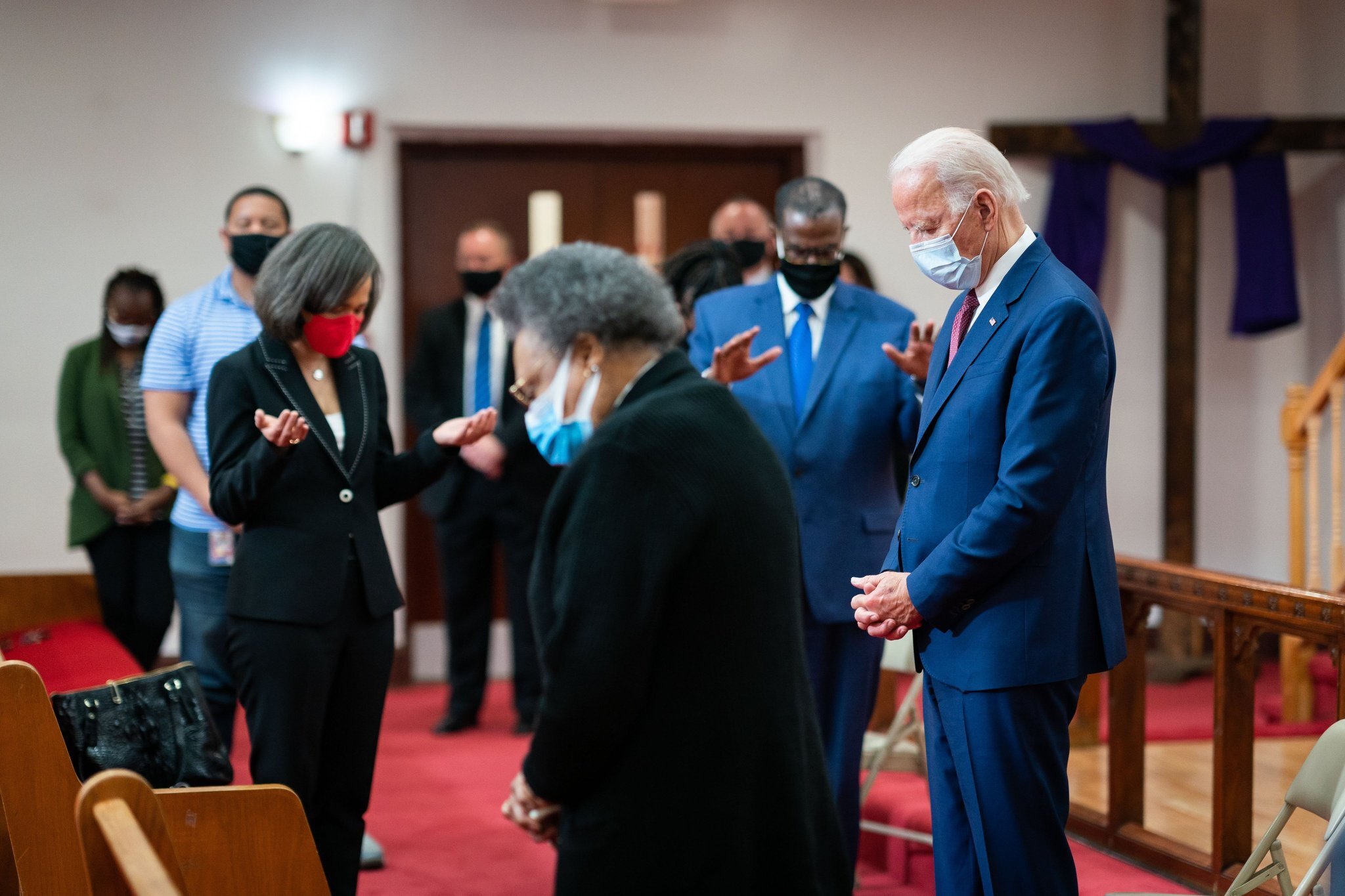 Rev. Silvester Beaman, Joe Biden and others stand inside a church with their heads down in prayer