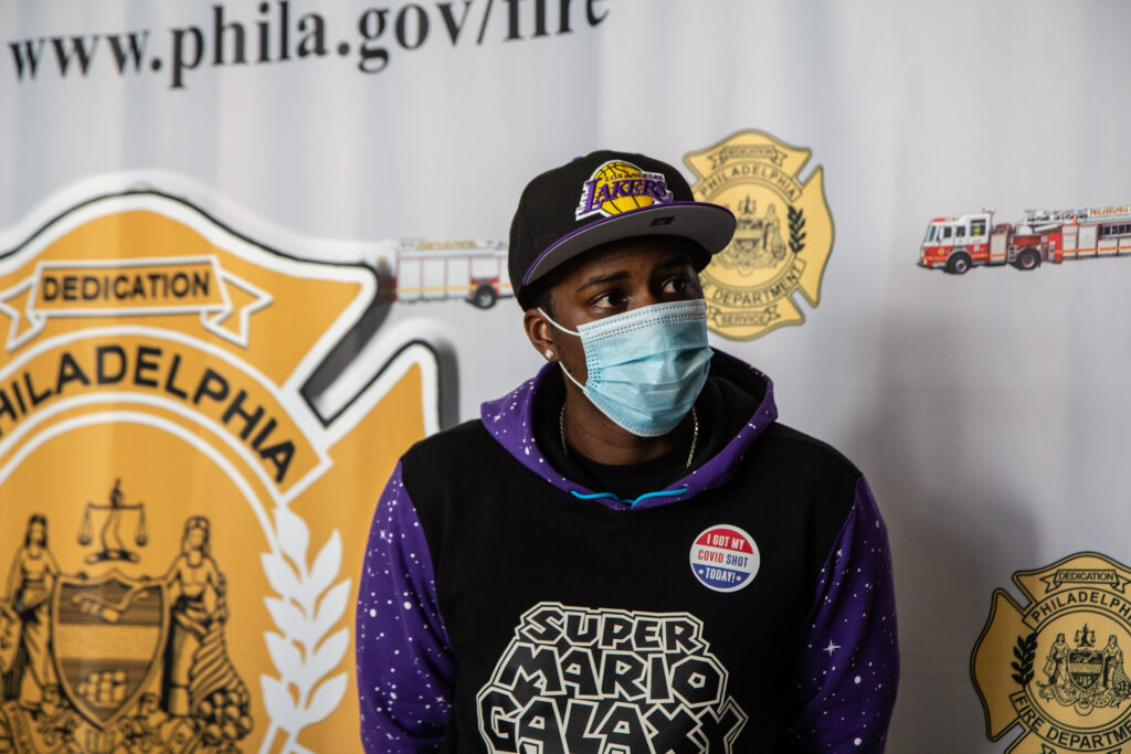 coronavirus_vaccine_PFD_KP_010621_01 Eric Crawford sits in front of a Philadelphia Fire Department banner while wearing a mask