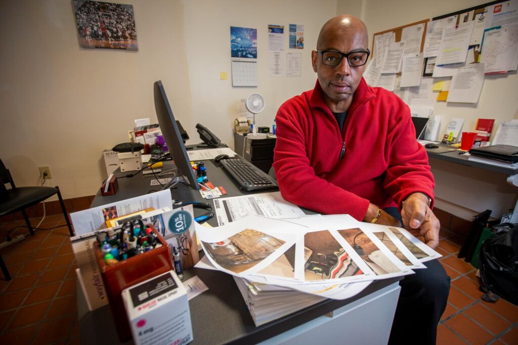 Fred Way sits at his desk with papers strewn across it.