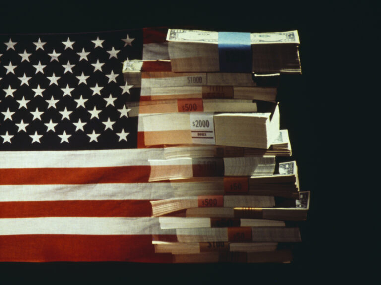The American flag superimposed over a pile of American dollars banknotes