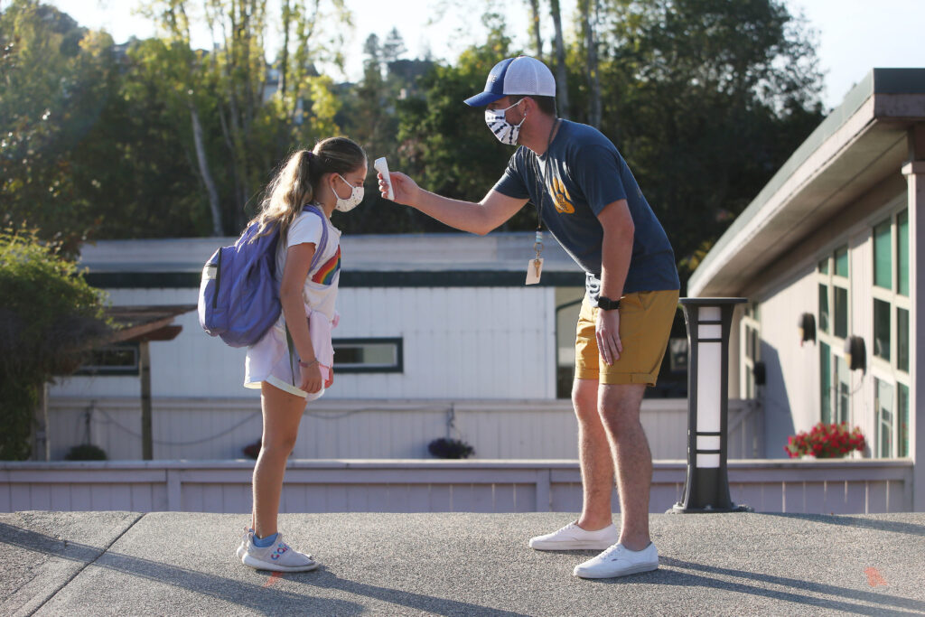 Nathan Grebil (right) takes the temperature of fourth-grade student Hyla during a health screening at Bel Aire Elementary School in Tiburon, Calif., in October. Nathan Grebil (right) takes the temperature of fourth-grade student Hyla during a health screening at Bel Aire Elementary School in Tiburon, Calif., in October.