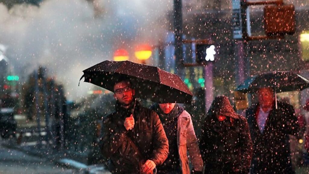 light_snow_NBC10_012621 A man holds an umbrella while crossing the street in the snow.